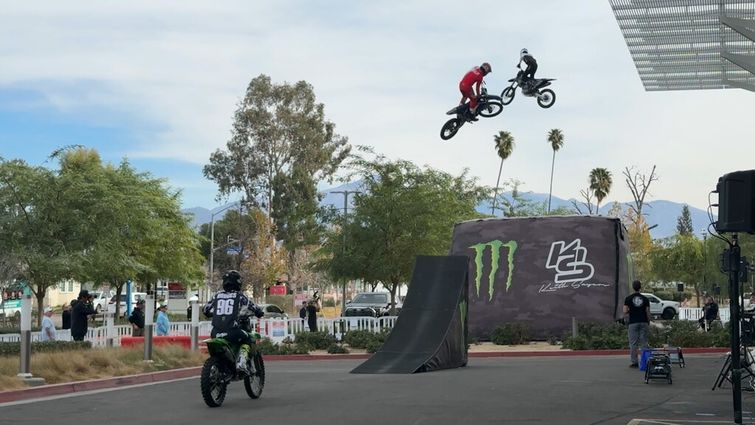 Three motocross riders doing tricks off ramp in front of Hospital for patients