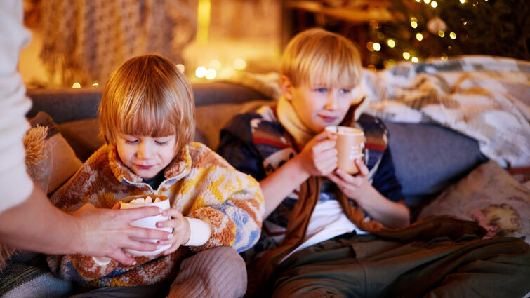 Two young boys sitting on a couch drinking hot chocolate 