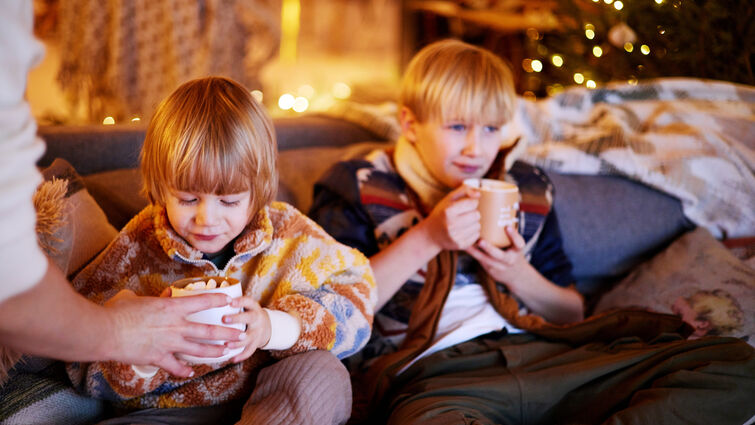 Two young boys sitting on a couch drinking hot chocolate 