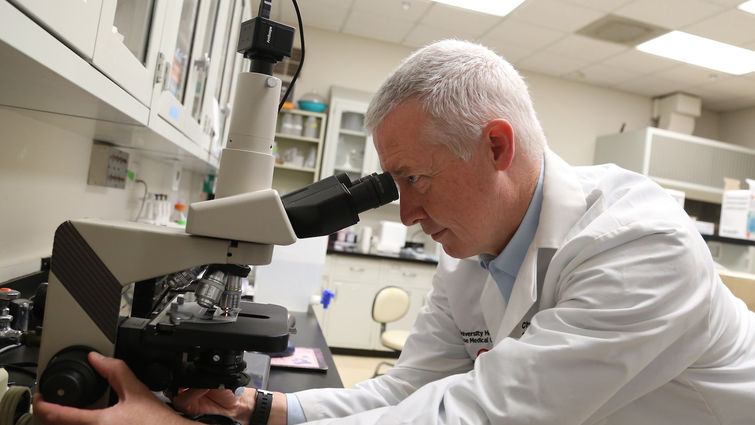 White male looking into a microscope inside a research lab
