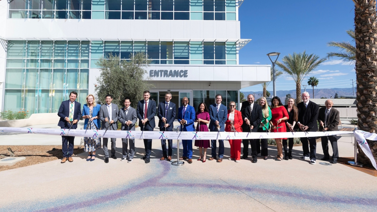 LLUH leaders pose for photo behind long ribbon with large scissors