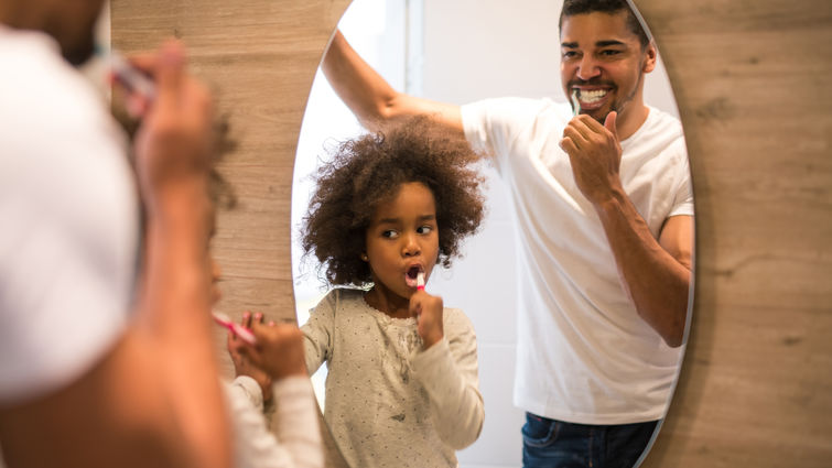 Father and daughter brush teeth in a mirror