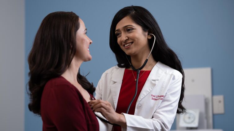 a woman doctor uses here stethoscope to examine a woman patient