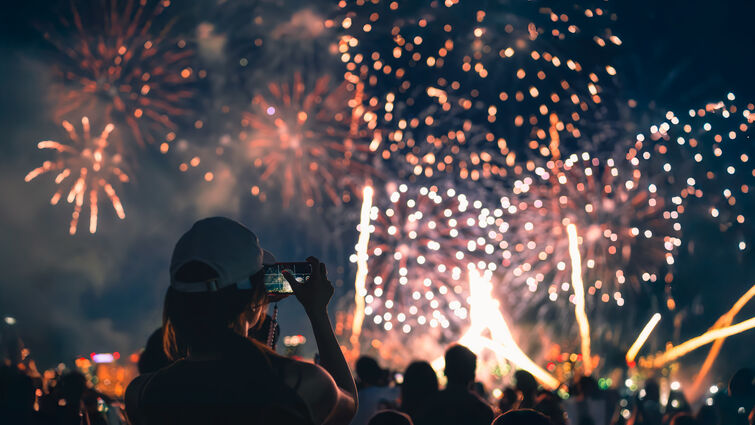  The back of a girl in a baseball cap filming a fireworks display on her mobile phone