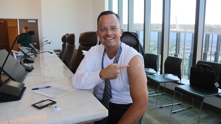 Man in white shirt points to bandaid on his arm