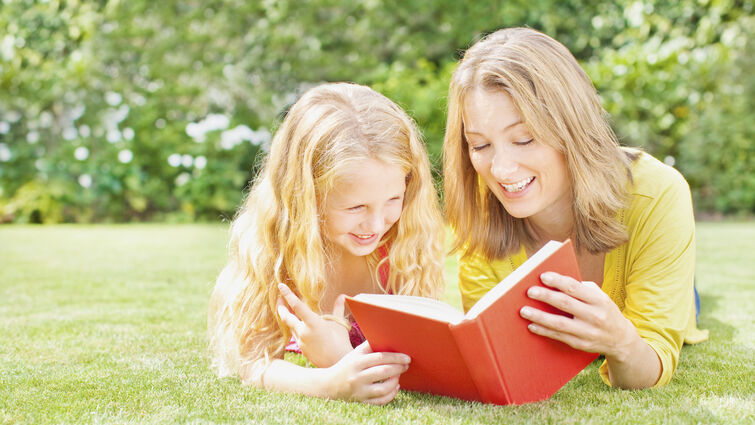Mother reading to daughter in backyard