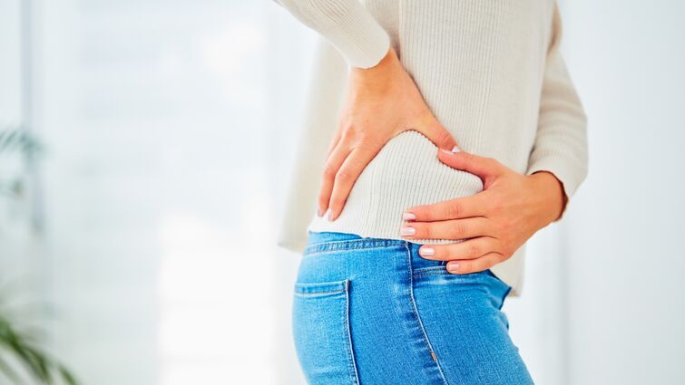 A woman in a white sweater and jeans holds her hip with pain