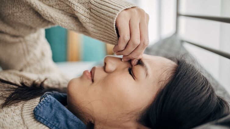 A woman having headache while lying on bed in her bedroom at home