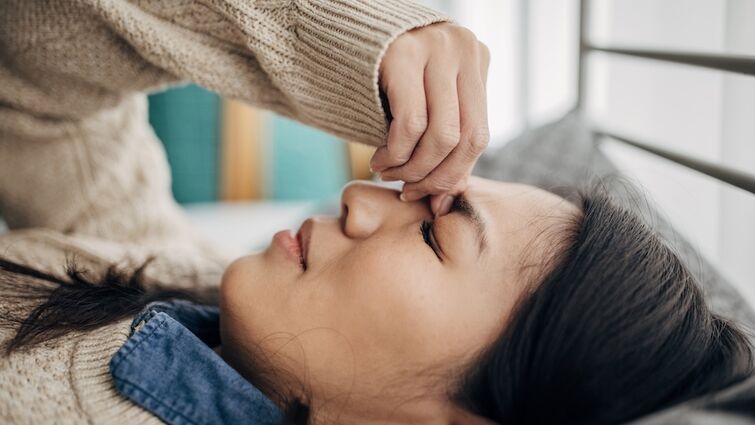 A woman having headache while lying on bed in her bedroom at home