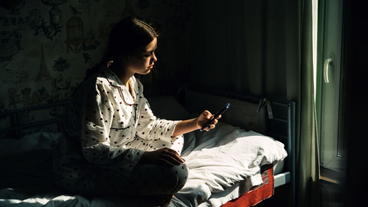 teenage girl looks at phone while in bed