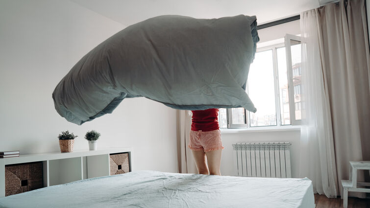  A woman makes her bed, the sheet billowing in the air above the mattress
