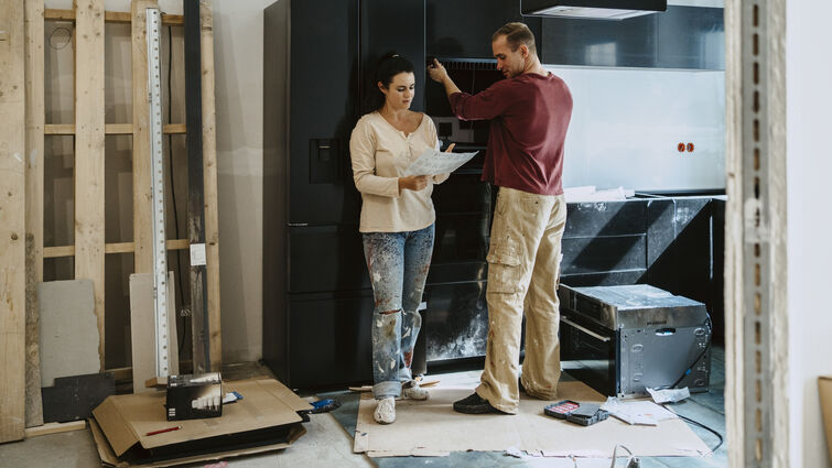 Couple discussing over document while fixing cabinet together in kitchen during home renovation