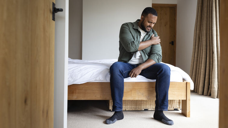 A mid adult man sitting on the edge of his bed in the bedroom at home