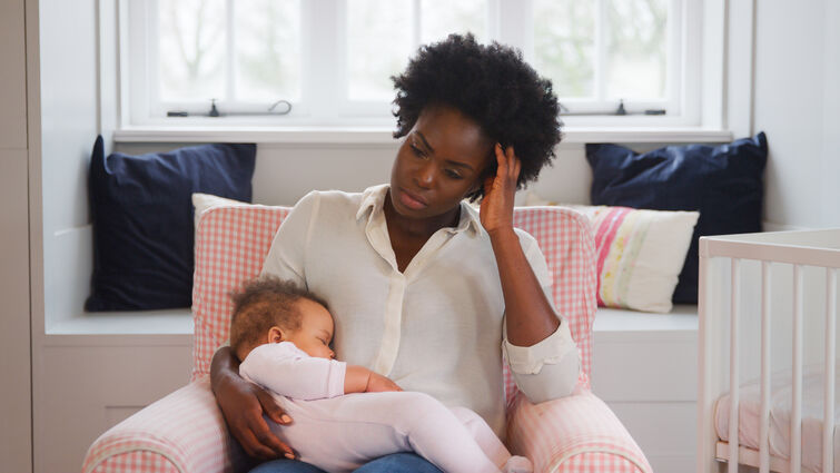 New Mother Suffering With Post Natal Depression Holding Sleeping Baby Daughter In Nursery At Home