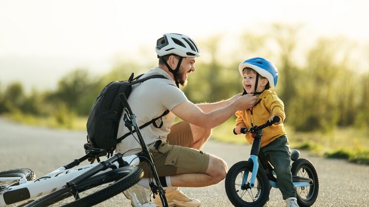 A father kneeling down to strap on a helmet for a young boy