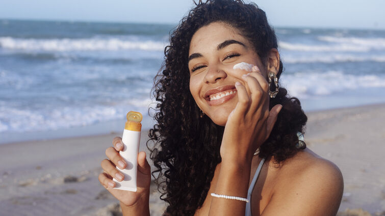 Young woman applying sunscreen on her face at the beach