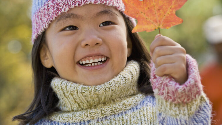 young girl smiles while holding fall leaf