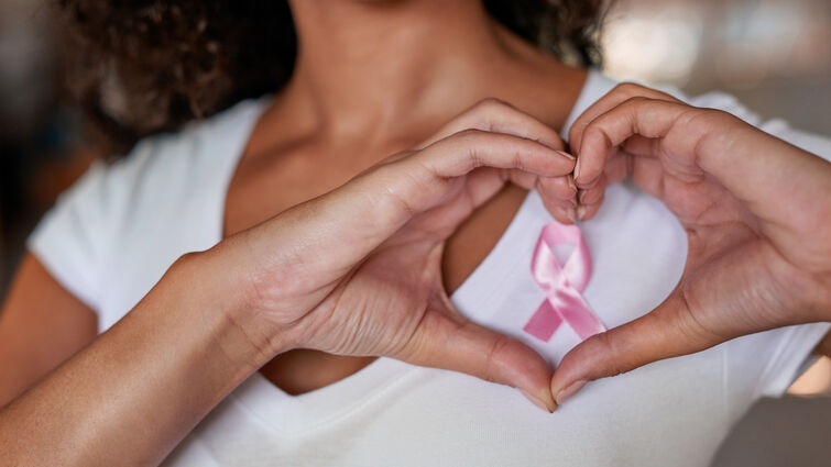 Women wearing pink ribbon on chest and making a heart with her hand