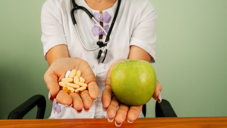 Woman displays a handful of pills versus a green apple.