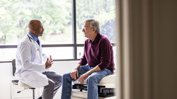 Male doctor talking with senior man in exam room - stock photo