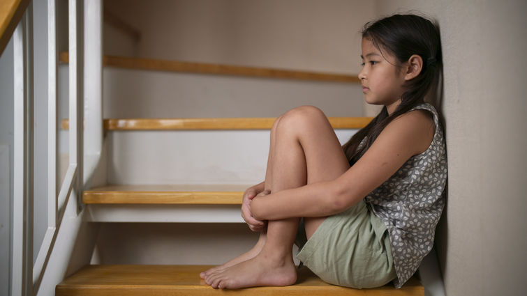 Little girl unhappy sad and sitting alone on staircase inside house
