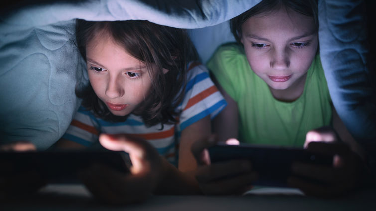 Boy and girl playing games on mobile phone in their bed stock photo