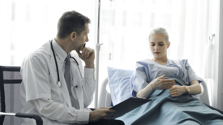 Doctor doing a physical examination of the young beautiful patient and explaining health problems to the patient who lying on the hospital bed, health care and hospital concept stock photo