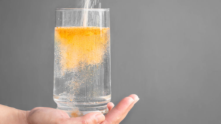Pouring orange powder, alluding to electrolyte supplements, into clear water glass
