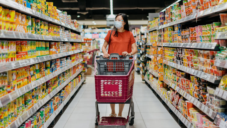 Woman shopping in supermarket aisle lined with processed foods