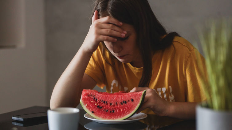 teen with hand on head in frustration while sitting at table in front of slice of watermelon