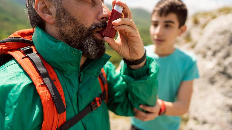 an inhaling himself with asthma inhaler, while his worried son giving him support, during their hike stock photo