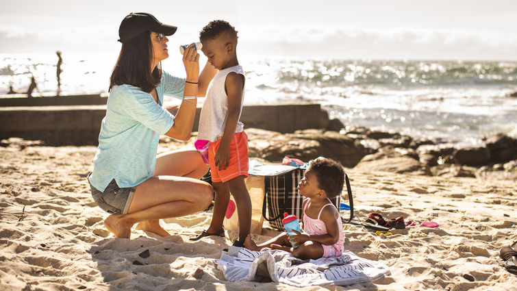 Mom putting suntan lotion on her little children at the beach stock photo