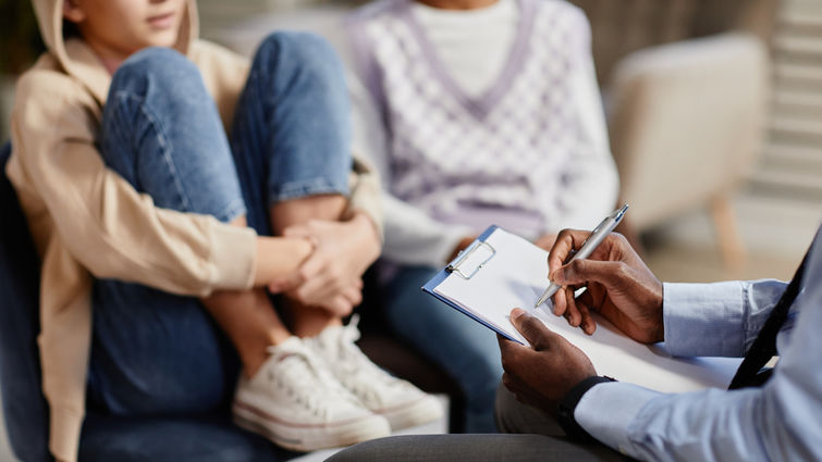 Close up of African-American psychologist taking notes on clipboard in therapy session for children