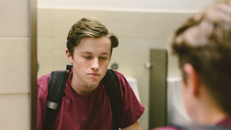 Depressed teen looks at himself in bathroom mirror stock photo