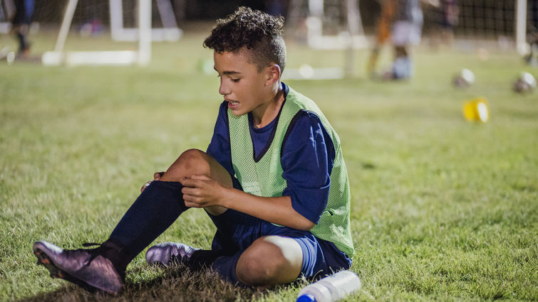 Young soccer player sitting on the grass nursing an injury.