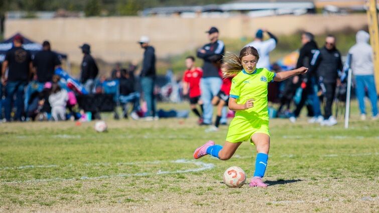 Young girl kicks soccer ball at sports game.