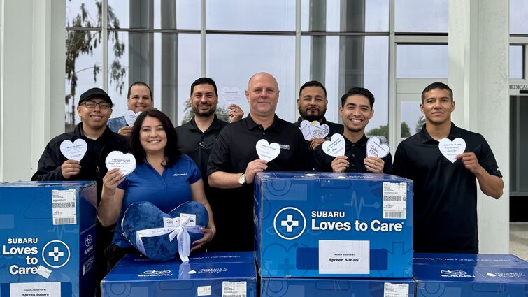 The Subaru Loves to Care team donated 80 blankets and care packages to patients at Children's Hospital on Tuesday, June 24. Group of individuals standing outside with blue boxes holding paper hearts.