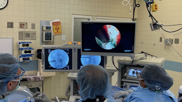 Three doctors in an operating room looking at the screen