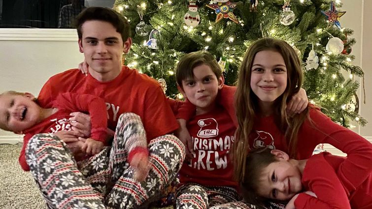 Elijah sitting with his siblings by Christmas tree