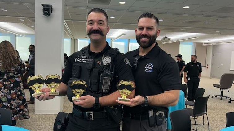 Two Upland police officers celebrate their agency's wins across multiple categories at the 2024 No-Shave November event. Two officers stand side by side holder trophies, smiling