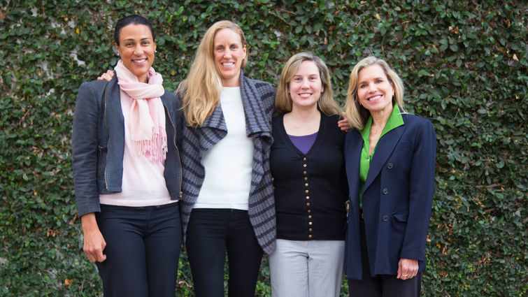 Four women smile in front of foliage