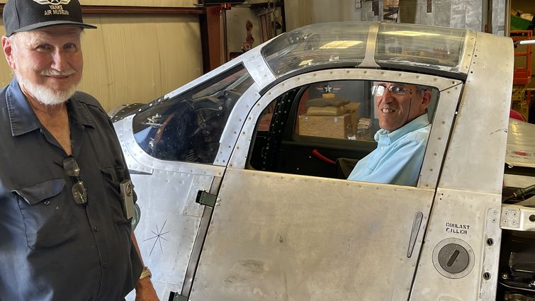 Joe Yancey shows Dr. Akhtari his hangar as Dr. Akhtari sits in a world war II plane cockpit