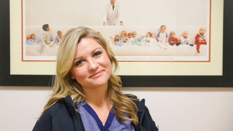 female nurse poses for photo in front of picture of Dr. Bailey and children he helped