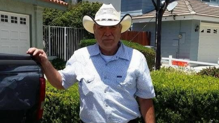 A person wearing a white cowboy hat stands beside a pickup truck on a sunny residential street.