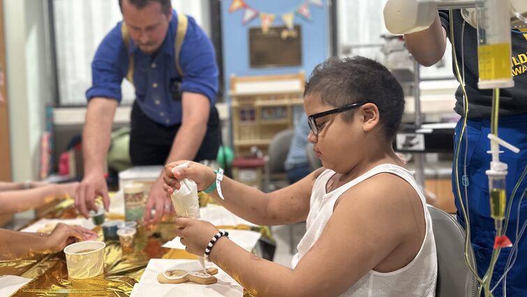 Pediatric cancer patient decorates ribbon-shaped cookie with frosting