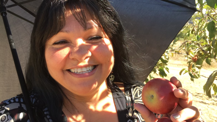 Regina Juarez smiles while holding apples picked from an apple orchard