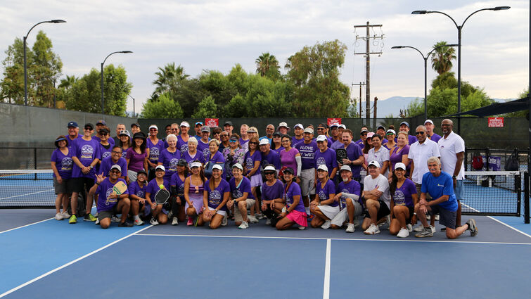 Attendees wearing purple shirts gather on pickleball court 