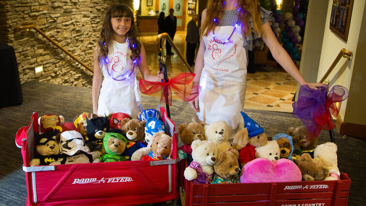 two young girls standing with red wagons full of teddybears 