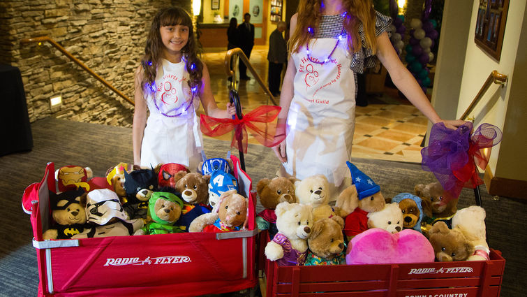 two young girls standing with red wagons full of teddybears 