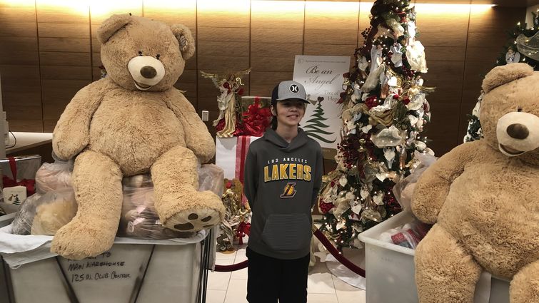 teenage boy standing with carts of teddy bears in hospital lobby